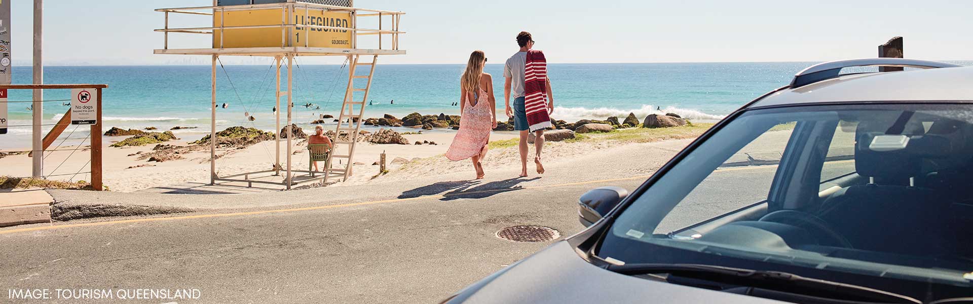 Couple walking away from rental car towards QLD beach
